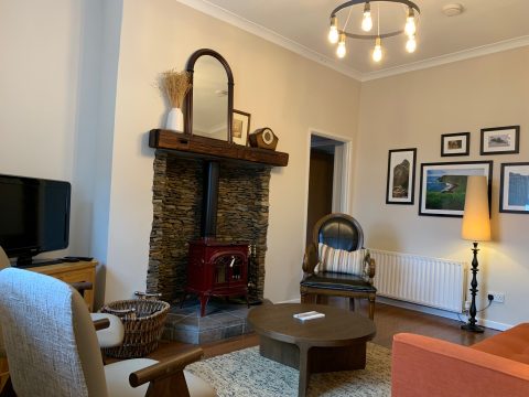 Red wood-burning stove set in a stone fireplace, with armchairs and framed Causeway Coast prints