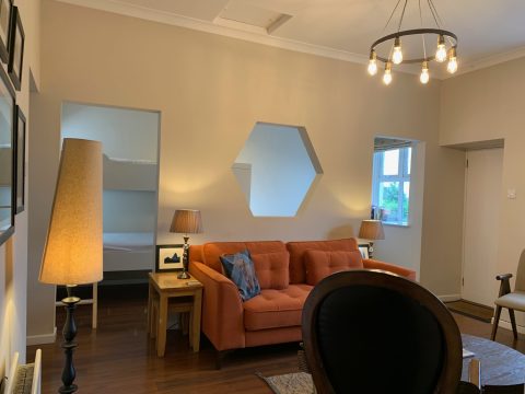 Open-plan living area with an orange sofa beneath a hexagonal mirror, beside the bunk-bed alcove